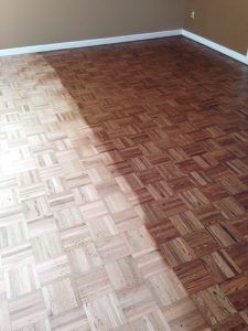 Parquet wood floor, half sanded to show light-colored wood compared to dark, finished side.
