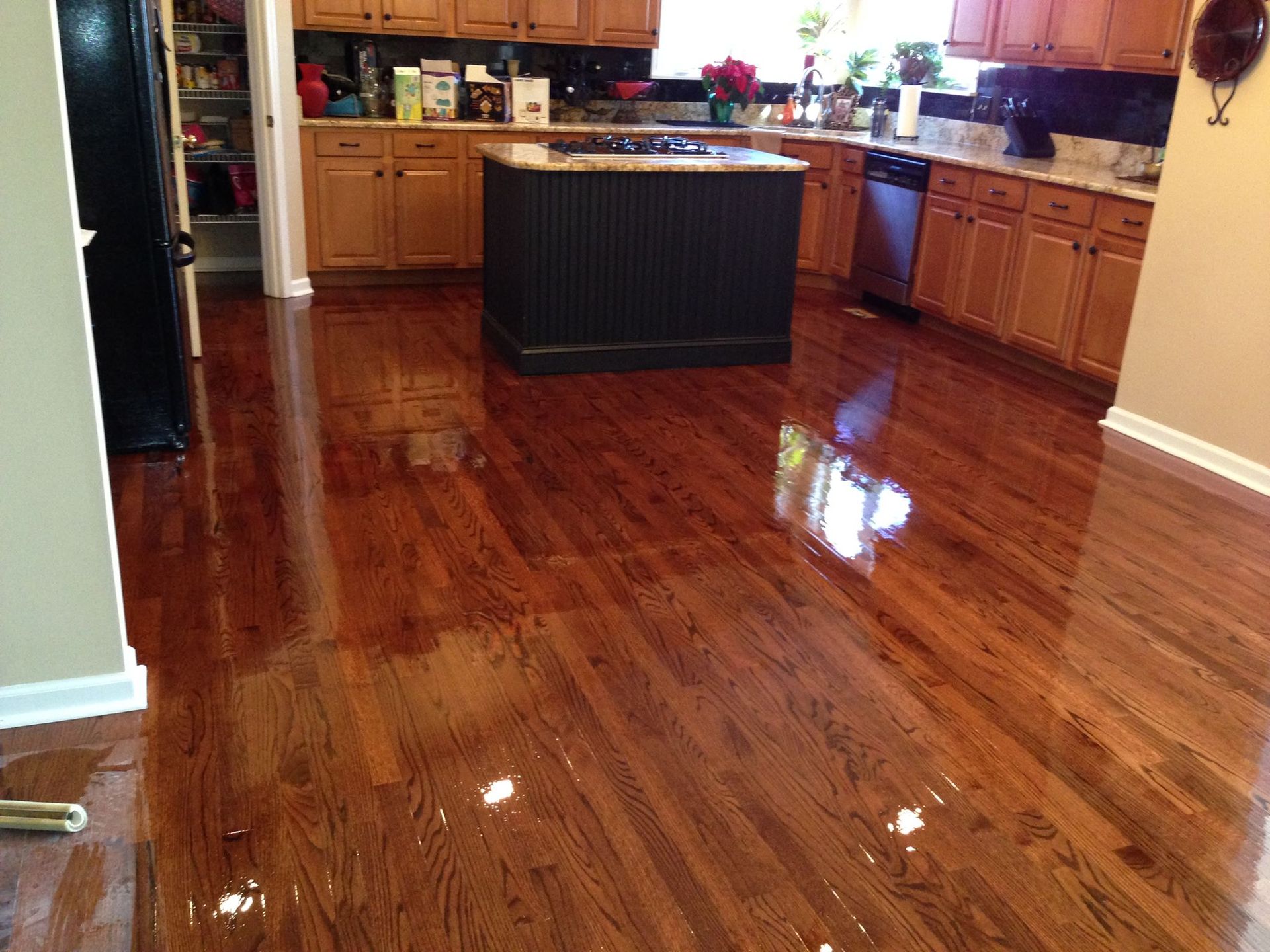 Shiny hardwood floor in a kitchen with a dark island and light wood cabinets.