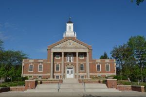 Brick building with columns and a steeple. Exterior shot on a sunny day. White doors and windows.