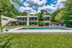 Modern white house with a pool, and green lawn. Blue chairs sit by the pool.